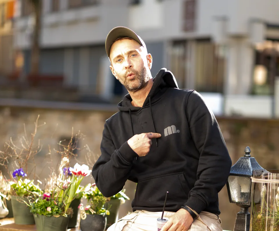 Markus Lauscher sitzt vor dem Laden auf einer Bank, umgeben von bepflanzten Töpfen